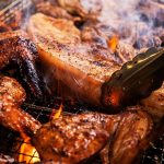 Chicken being grilled, a piece is being flipped over by a pair of tongs