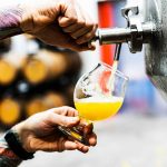 A bartender is pouring alcohol into a glass from a stainless steel keg