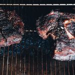 well seasoned steaks on the wire rack of a charcoal grill