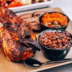 A platter with grilled chicken and sides of baked beans and sweet potato
