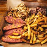 A paper lined tray with french fries, shredded chicken, smoked sausage, and rib meat