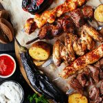a platter of grilled meat kebabs. there are multiple sauce options on the side